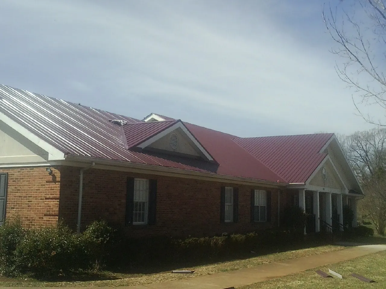 Red metal roof with gabled entries on a long brick building, from a Hail Damage Roof Repair job in Scottdale