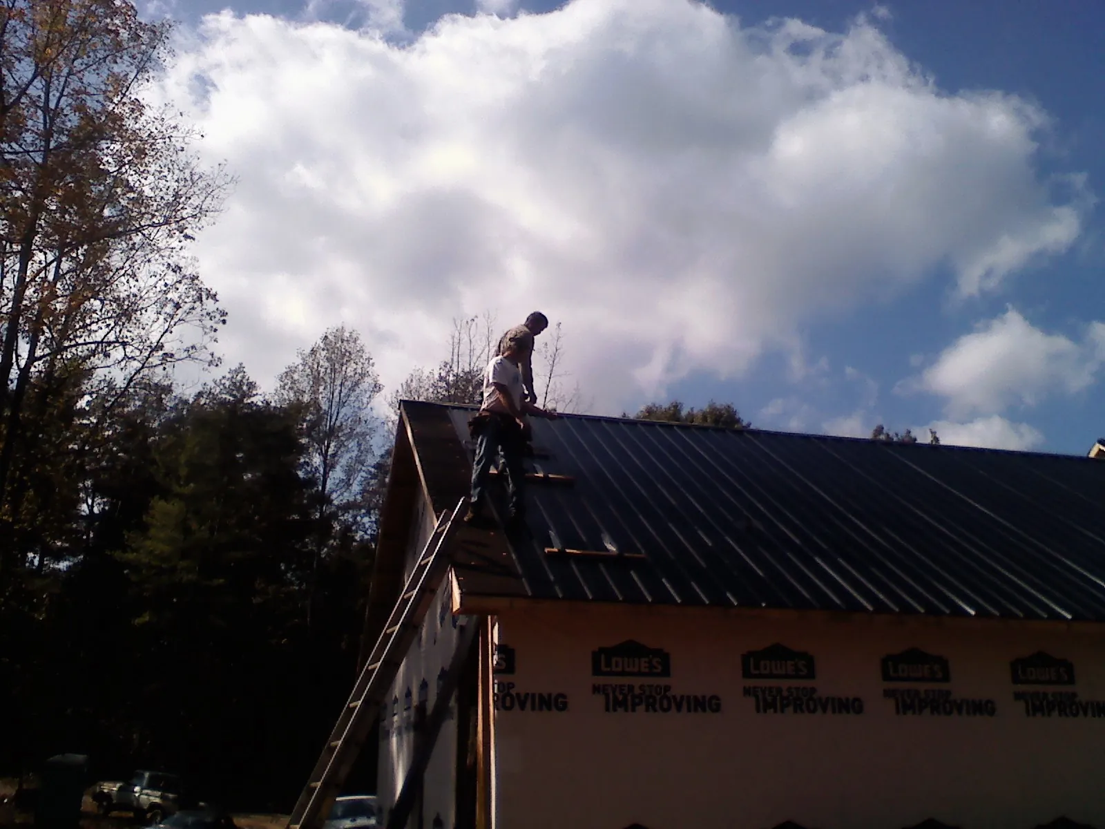 Roofer fastening dark metal panels high against a cloudy sky, from a Roof Inspection job in Scottdale